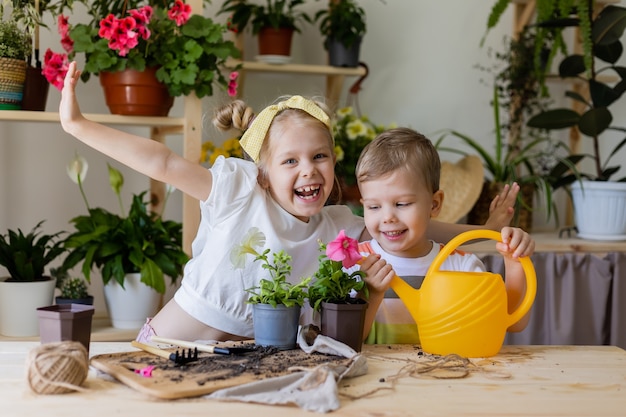 Een jongen en een blond meisje planten en planten bloemen binnen en geven ze water uit een gele gieter
