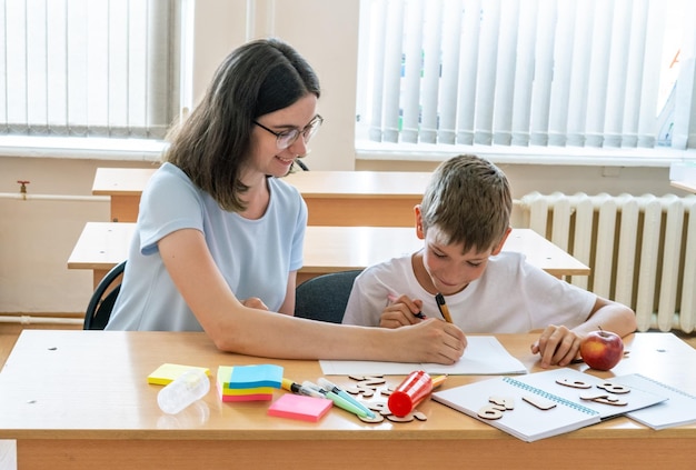 Een jongen en een leraar doen huiswerk en schrijven tekst in een notitieboekje aan tafel Een moeder helpt haar zoon om in een notitieboekje te schrijven