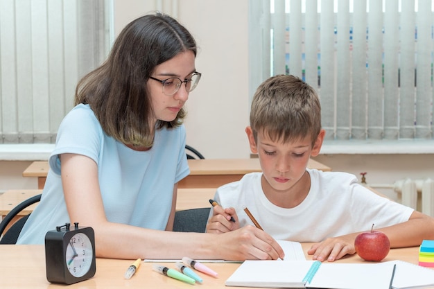 Een jongen en een leraar doen huiswerk en schrijven tekst in een notitieboekje aan tafel Een moeder helpt haar zoon om in een notitieboekje te schrijven