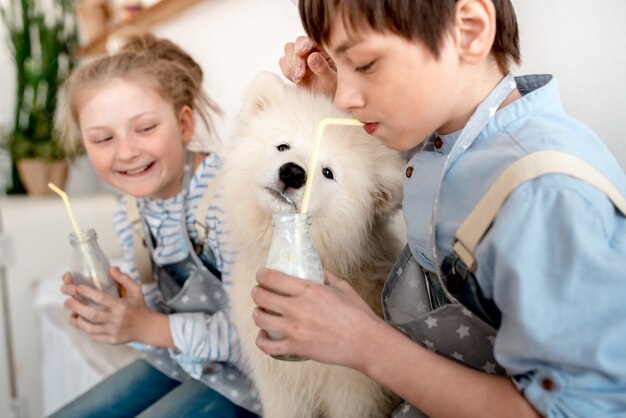 Een jongen en een meisje drinken melk met een rietje, en een puppy likt druppels uit een fles