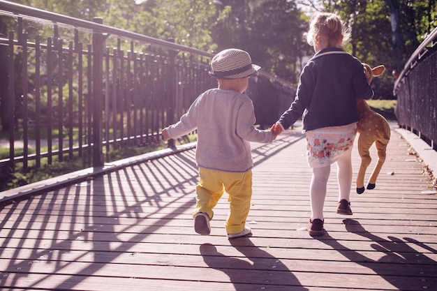 Een jongen en een meisje lopen hand in hand over een brug.