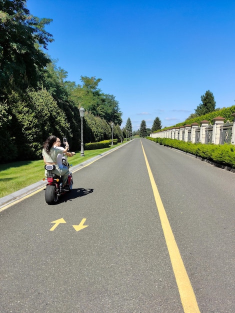 Een jongen en een meisje rijden op een elektrische scooter in perspectief op de weg in een stadspark.