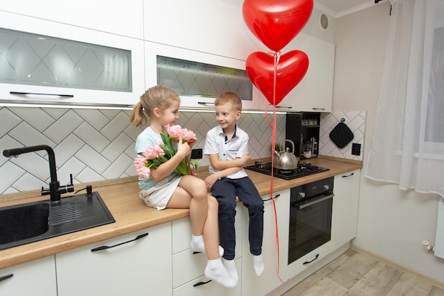 Een jongen en een meisje zitten op een keuken met een boeket roze tulpen Gelukkig romantisch paartje