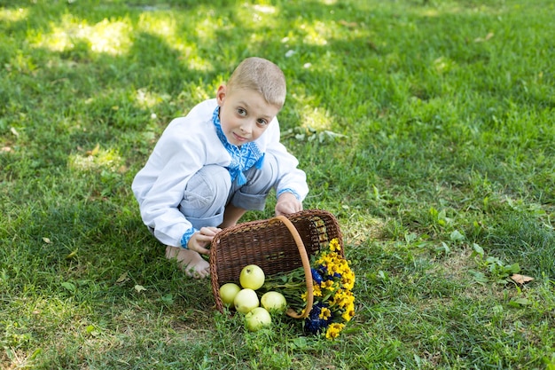 Een jongen geknield op het gras met een mand vol bloemen.