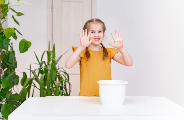Een jongen groezelig grappig meisje toont handen besmeurd met bloem. culinaire hobby voor kinderen.