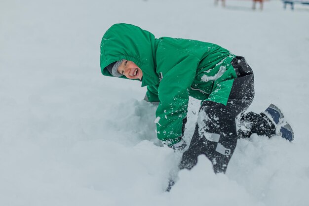 Foto een jongen in een groene jumpsuit viel in de sneeuw de jongen speelt in de sneeuw kind speelt buiten in de winter