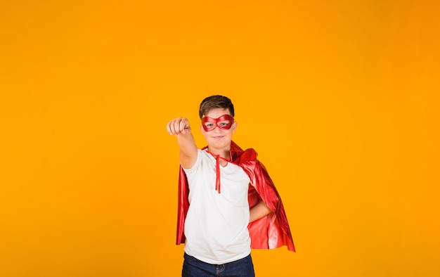 Een jongen in een heldenkostuum en een masker staat op een gele achtergrond met een plek voor tekst