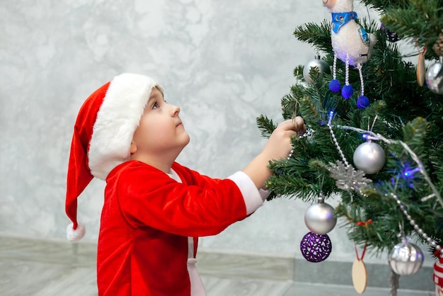 Een jongen in een kerstmankostuum versiert een kerstboom