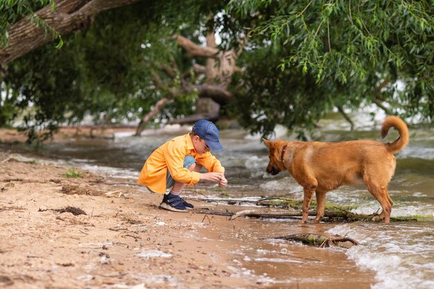 Een jongen in een oranje shirt speelt met een rode hond aan de kust