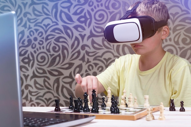 Een jongen in een virtual reality-headset schaakt met een laptop Leren schaken met behulp van informatietechnologie