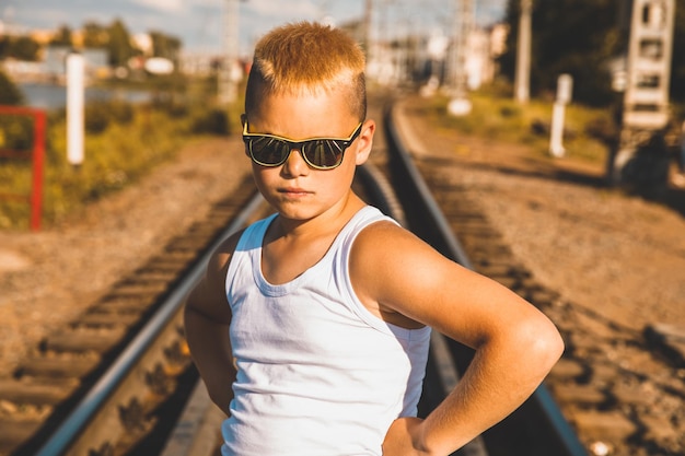 Een jongen in een wit T-shirt en een zwarte bril staat op het spoor. bruine toning