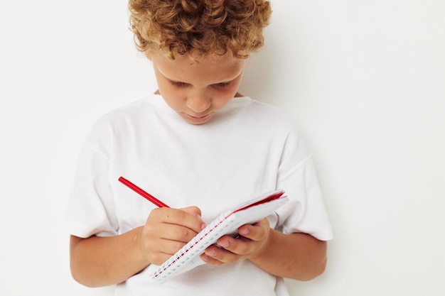 Een jongen in een wit t-shirt tekent met een potlood in een notitieboekje