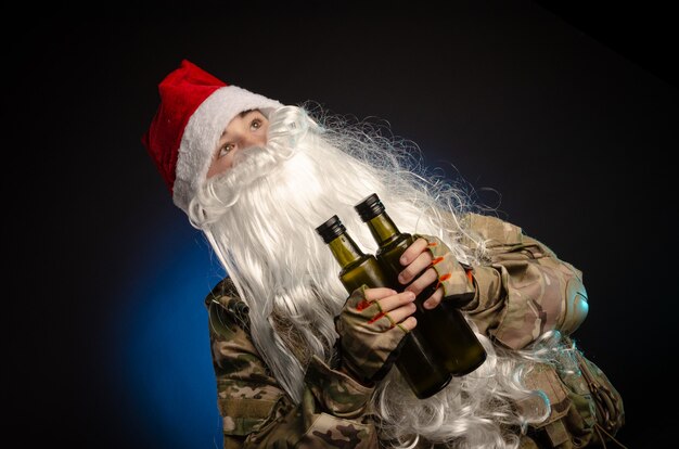 Een jongen in militair uniform met een baard en een kerstmuts die een fles vasthoudt