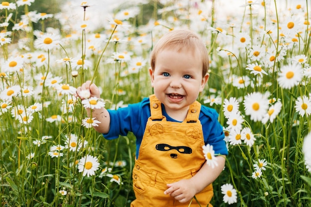 Een jongen met blauwe ogen en blonde haren staat in een bloemrijke weide met kamillebloemen en glimlacht