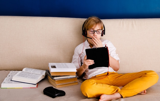 Een jongen met bril en koptelefoon leert lessen met een tablet en boeken