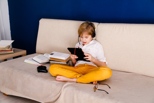 Een jongen met bril en koptelefoon leert lessen met een tablet en boeken