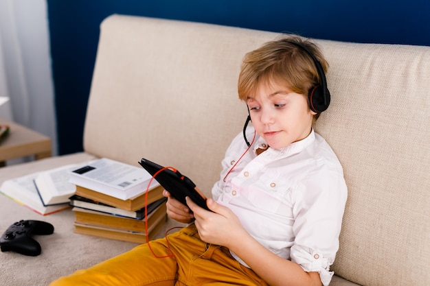 Een jongen met bril en koptelefoon leert lessen met een tablet en boeken