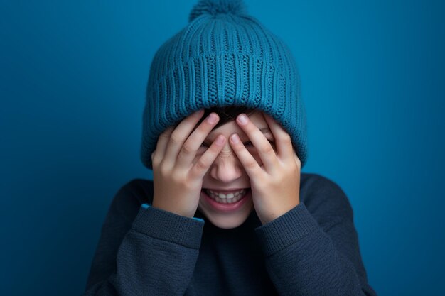 een jongen met een blauwe gebreide muts lacht op een blauwe achtergrond