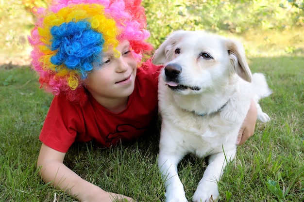 Een jongen met een clownpruik knuffelt een hond.