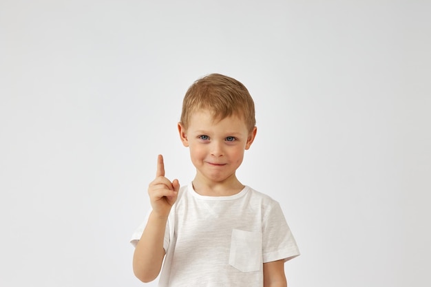 Een jongen met een grappig gezicht wijst zijn vinger omhoog op een witte achtergrond