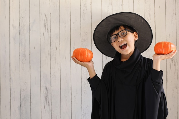 Foto een jongen met een grappige uitdrukking die een halloweenkostuum draagt en pompoenen vasthoudt