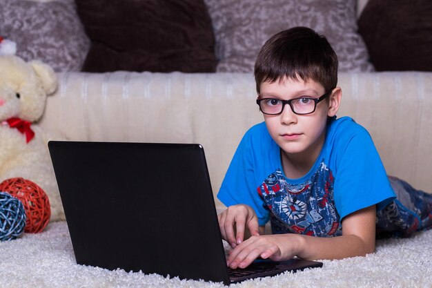 Een jongen met een laptop die thuis op de vloer ligt op het tapijt Technologie Internet modern communicatieconcept