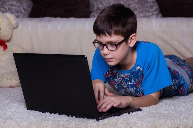 Een jongen met een laptop die thuis op de vloer ligt op het tapijt Technologie Internet modern communicatieconcept