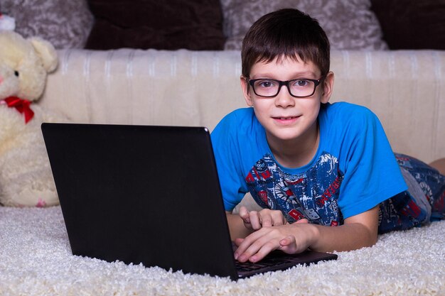 Een jongen met een laptop die thuis op de vloer ligt op het tapijt Technologie Internet modern communicatieconcept
