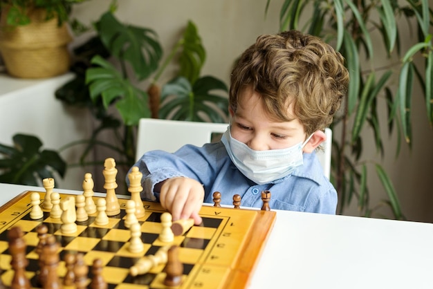 een jongen met een medisch masker speelt thuis schaakactiviteiten