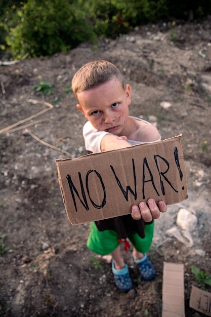 Een jongen met een vuil gezicht en droevige ogen houdt een kartonnen poster vast met het opschrift NO WAR in het Engels