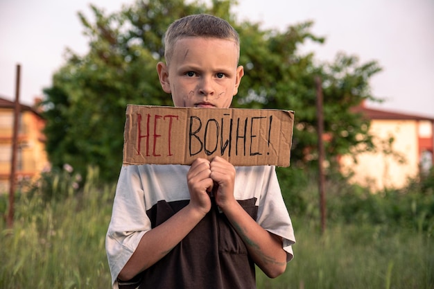 Een jongen met een vuil gezicht en droevige ogen houdt een kartonnen poster vast met het opschrift NO WAR