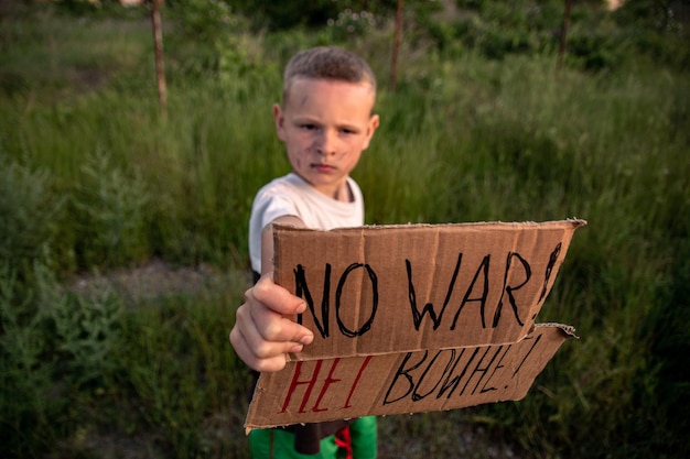 Een jongen met een vuil gezicht en droevige ogen houdt een kartonnen poster vast met het opschrift no war