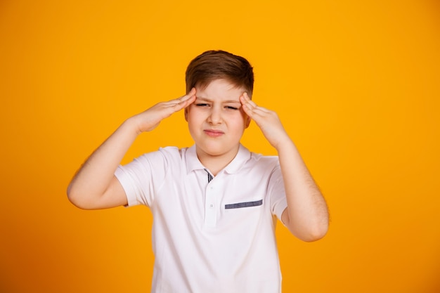 Een jongen met hoofdpijn. kaukasisch kind op een gele achtergrond die aan hoofdpijn en migraine lijden.