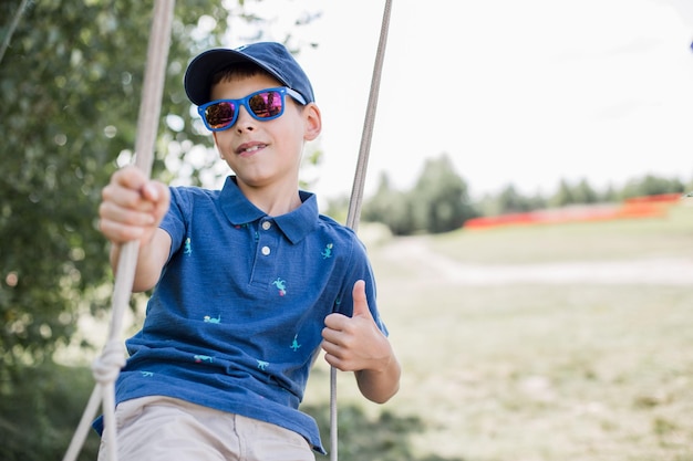 Een jongen met zonnebril rijdt in de zomer op een schommel in het park