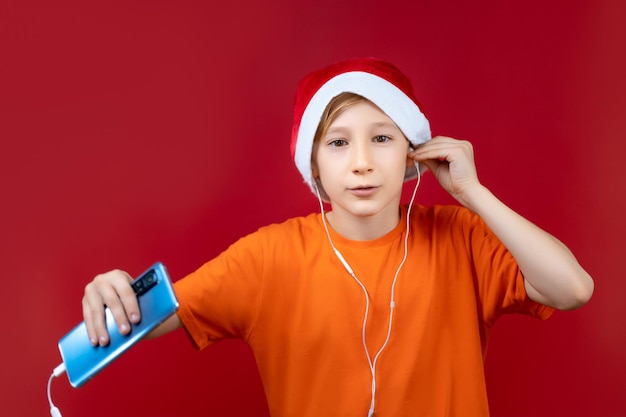 Een jongen op een kerstboom op een rode achtergrond en een kerstmuts houdt een muzikale oortelefoon vast