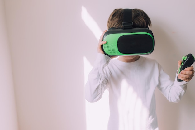 Een jongen speelt een vr-bril op een witte copyspace-muur Een artikel over moderne gadgets Een artikel over moderne technologieën