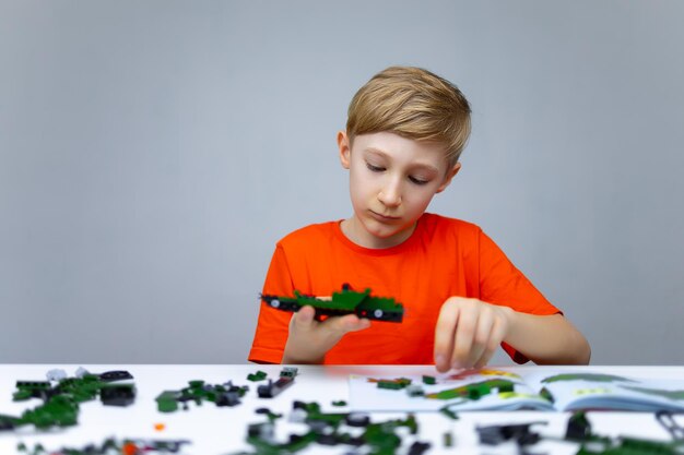 Een jongen speelt met een plastic constructeur die naar het montagemodel kijkt om het onderdeel te bevestigen