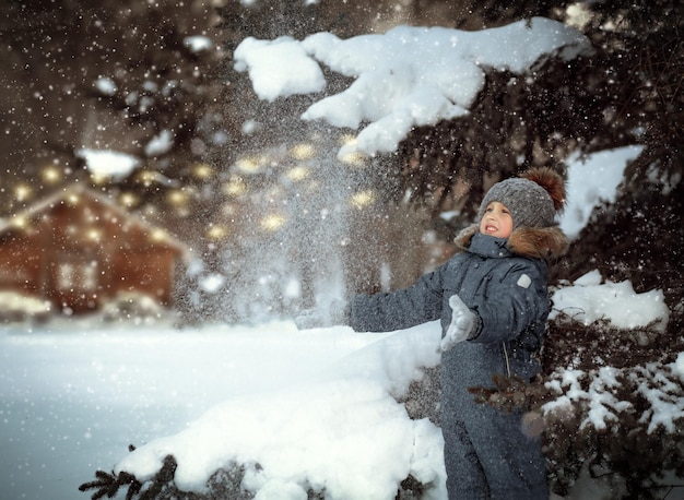 een jongen staat in een winters besneeuwd bos tussen de dennenbomen