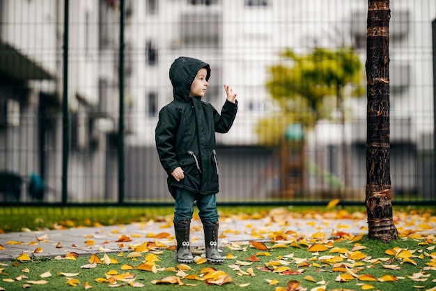 Een jongen staat in het stadspark in de regen en zwaait naar iemand