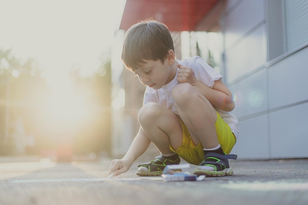 Foto een jongen tekent een levensstijl met kleurpotloden op het asfalt kinderlessen kindertekeningen kinderpsychologie