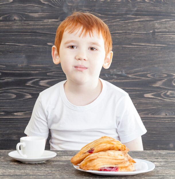 Een jongen tijdens het eten van een dessert gemaakt van een wit broodje van tarwekoekjes met rode kersenjam, op een zwarte