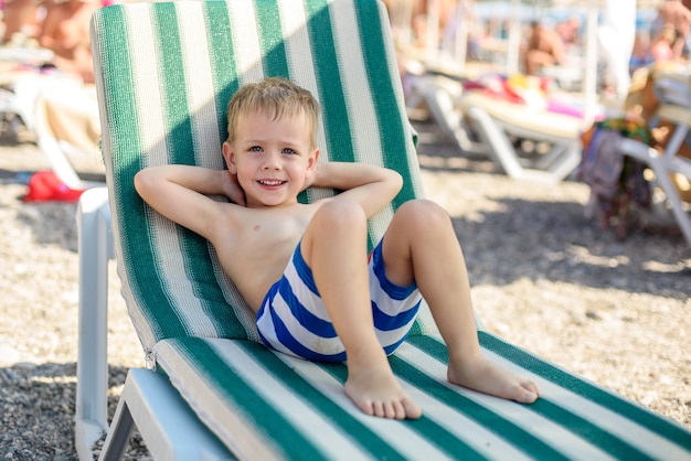 een jongen van 4 jaar oud in gestreepte korte broek ligt op een zonnebank op het strand tevreden en gelukkig Summer