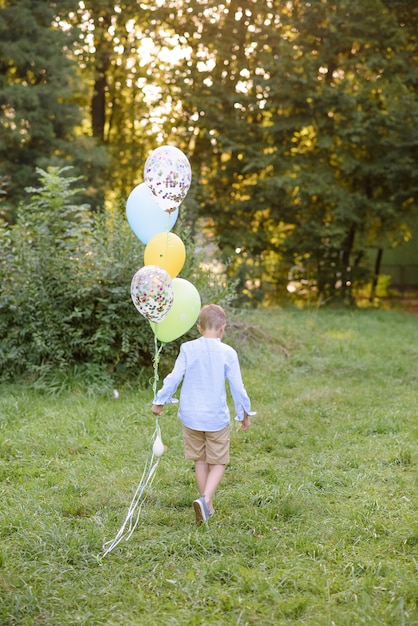 Een jongen van de basisschoolleeftijd rent met ballonnen. De jongen wijst met zijn rug naar de camera.