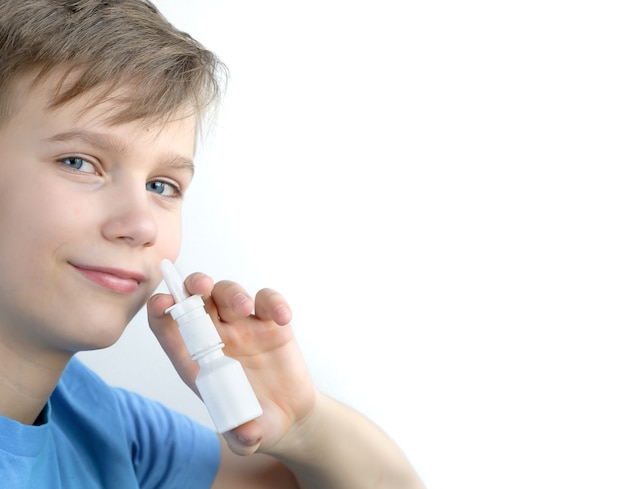 Een jongen van twaalf jaar spuit neusspray. Tiener in blauw shirt met neusspray in goed humeur