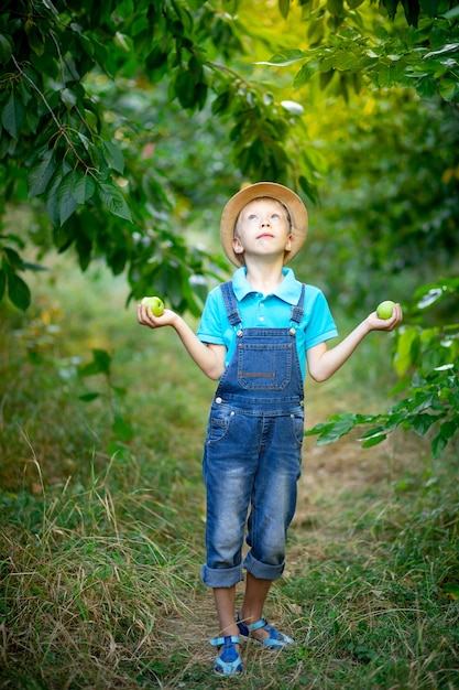 Een jongen van zes jaar staat in een tuin met appelbomen die omhoog kijken en appels in zijn handen houden