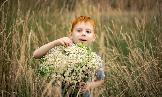 Een jongen van zeven met rood haar met een groot boeket wilde bloemen in de zomer