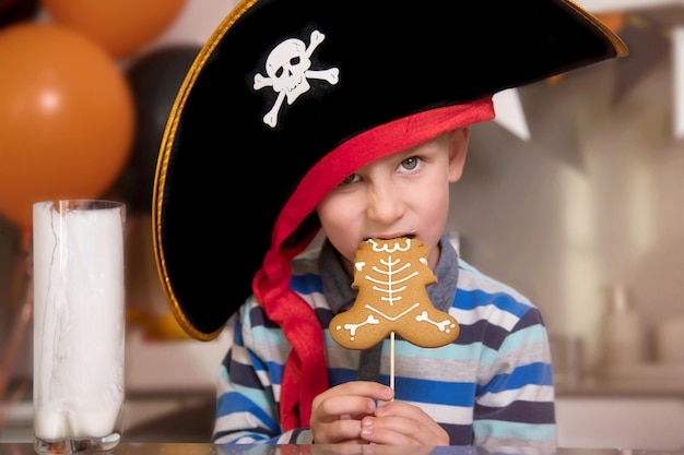 Een jongen verkleed als een piraat eet peperkoek terwijl een Halloween-skelet melk drinkt