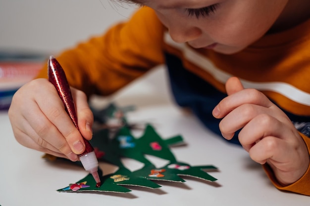 een jongen versiert papieren kerstbomen voor Kerstmis