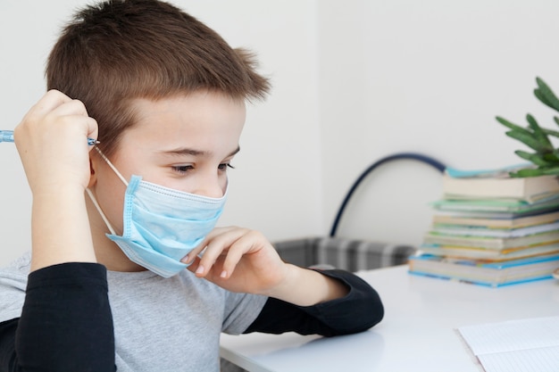 Een jongen zet een medisch masker op zijn gezicht. Thuisonderwijs in quarantaine plaatsen tijdens coronavirus