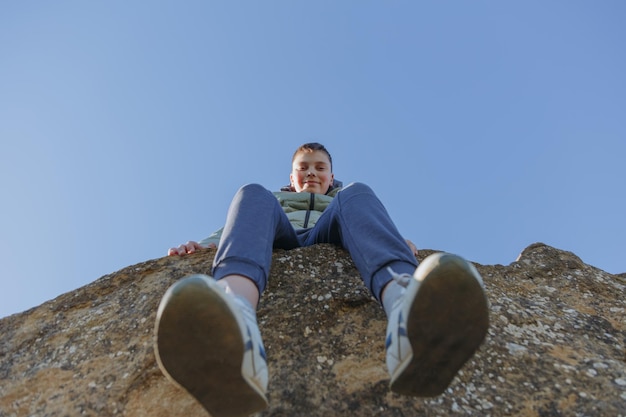Een jongen zit op een rots en kijkt omhoog naar de lucht.